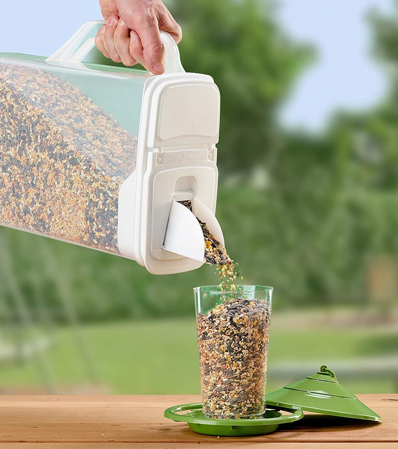 A person using the pet food bin to pour bird seed into a glass