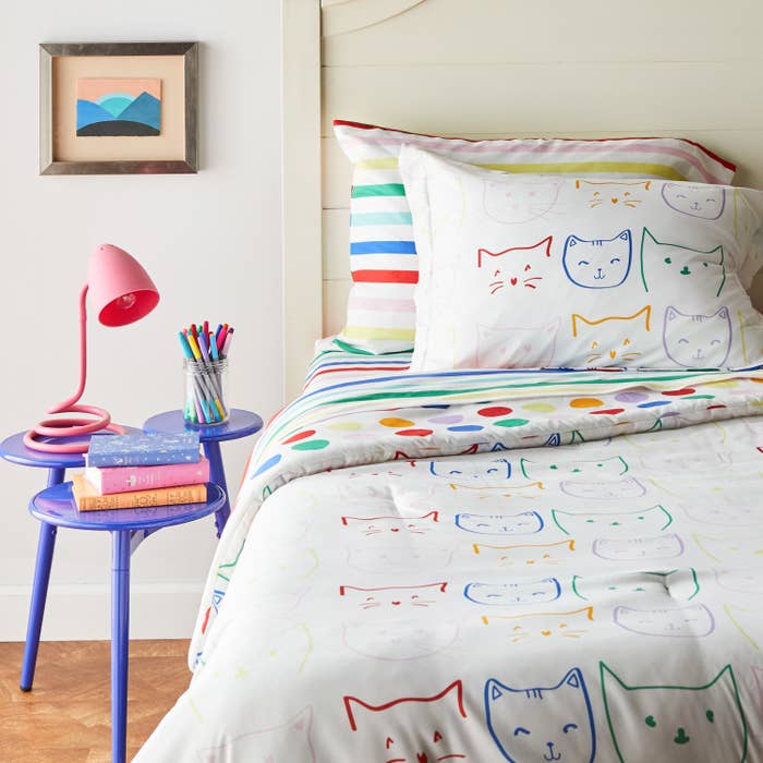 Red, blue, green, pink, purple, and yellow sketches of cat faces on white bedding