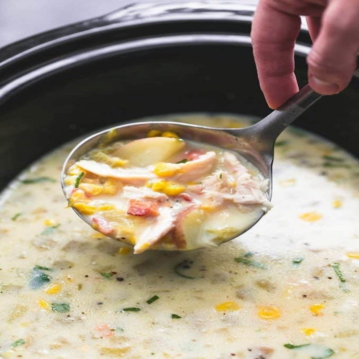 A ladle taking a scoop of creamy chicken and corn chowder with little bits of bacon and potatoes.