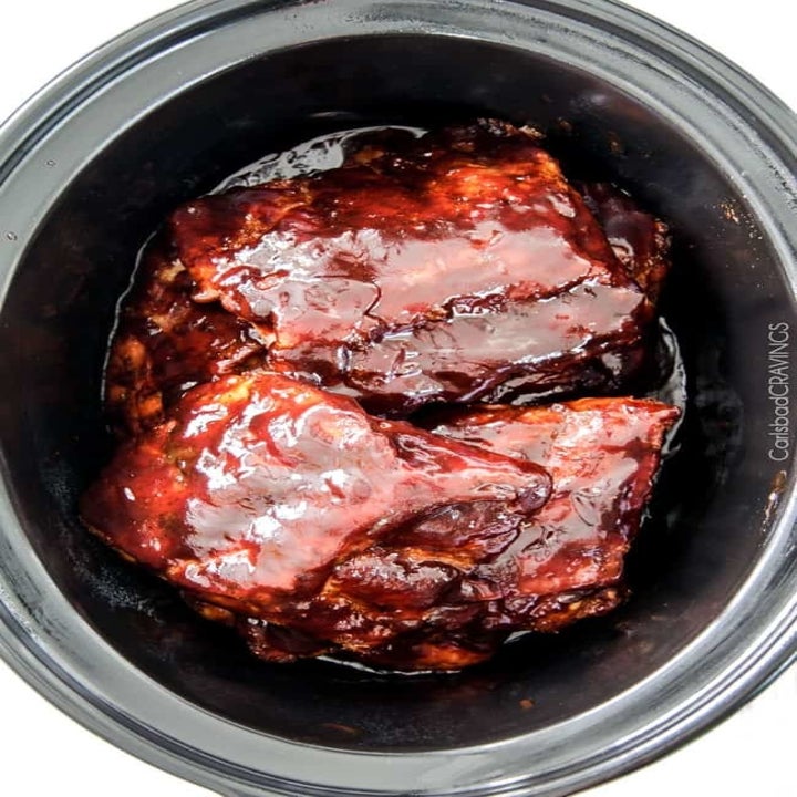 Half racks of ribs topped with barbecue sauce in the slow cooker.