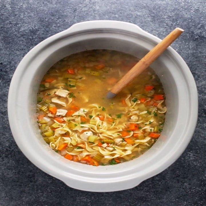 A slow cooker full of chicken noodle soup with egg noodles and diced veggies.