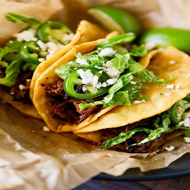 Three barbacoa beef tacos in tortillas with queso fresco, lettuce, and jalapeño.