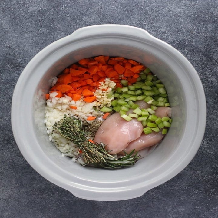 Ingredients for chicken noodle soup in the slow cooker —chicken breasts, diced celery, carrots, onion, and herbs.