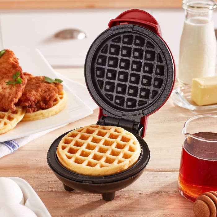 mini red waffle maker on a table top with chicken and waffles in the background