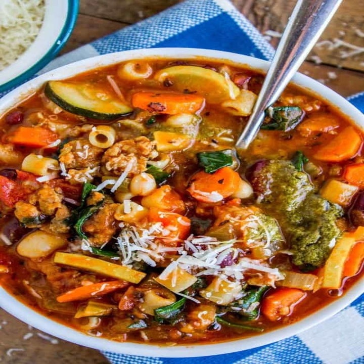A bowl of Minestrone soup topped with pesto and shredded Parmesan.