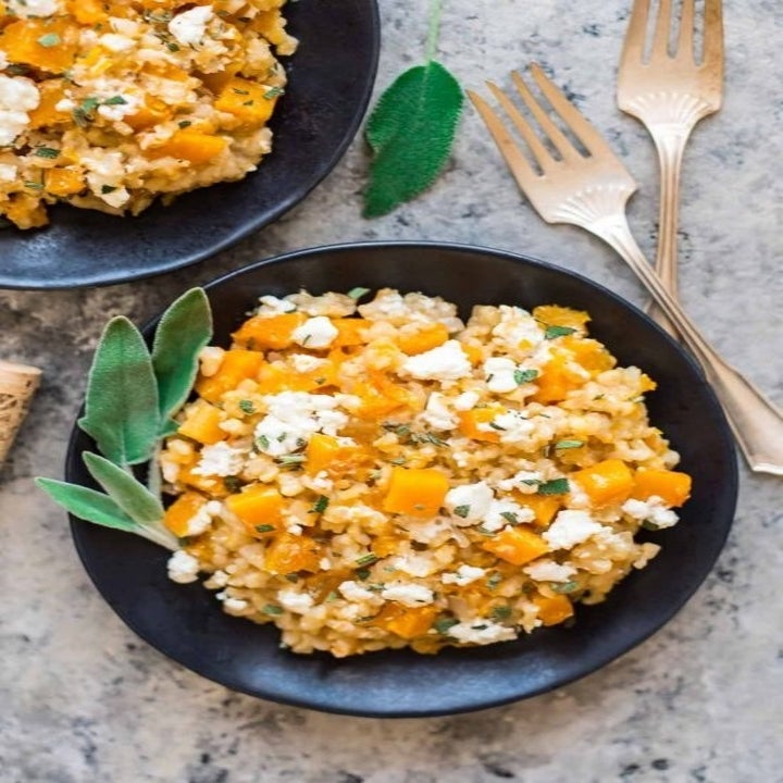 Two bowls of butternut squash risotto topped with goat cheese and sage leaves.