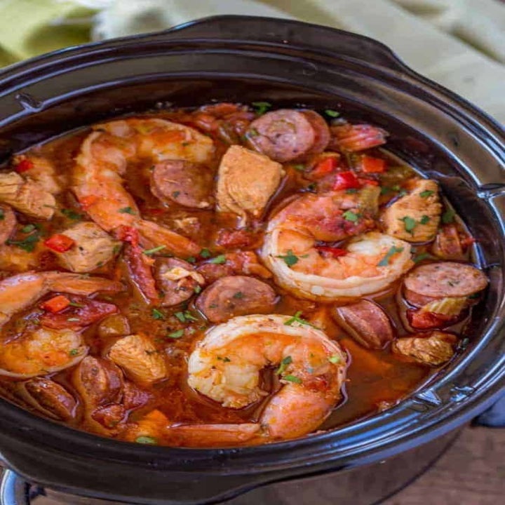 A slow cooker filled with cooked shrimp, sausage, chicken, and veggies in a tomato broth.