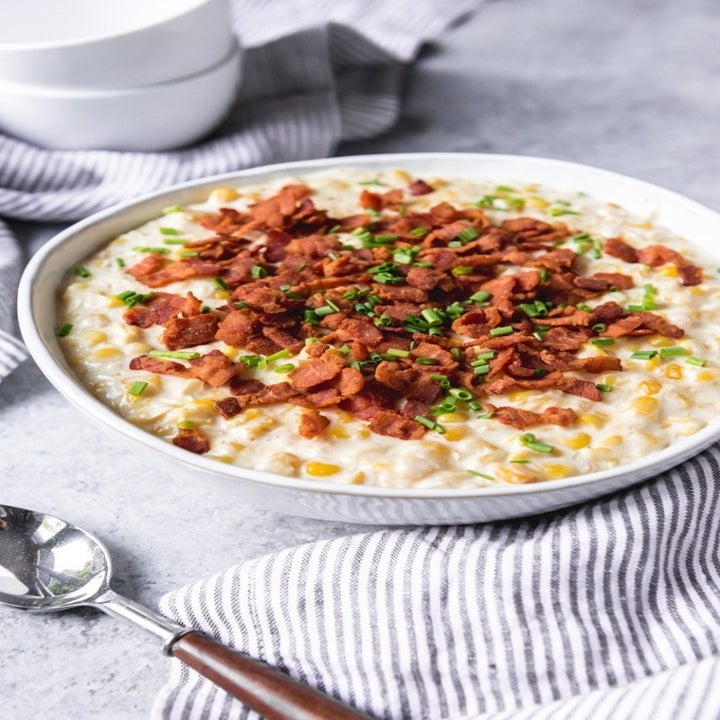 A bowl of super creamy corn with fresh scallions and bacon bits on top.