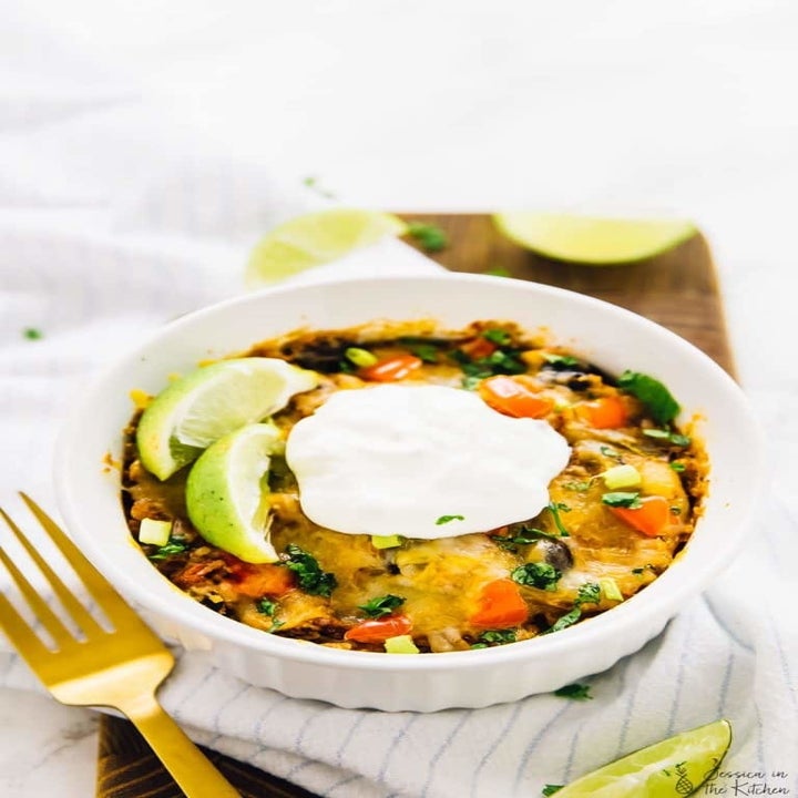 A ramekin filled with quinoa enchilada casserole and topped with a dollop of sour cream.