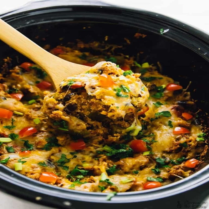 A wooden spoon taking a scoop of cheesy quinoa enchilada casserole.