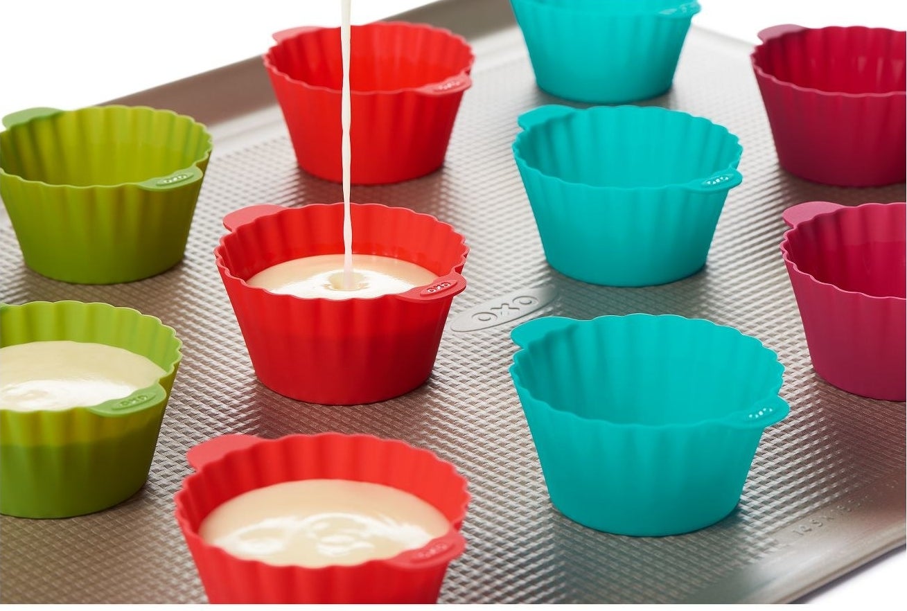 batter being poured into a red silicone baking cup with other baking cups on a baking sheet