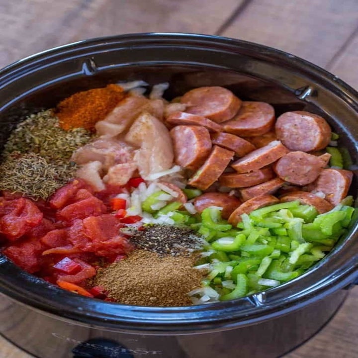 Sliced sausage, diced chicken breast, vegetables, spices, and diced tomatoes in a slow cooker.