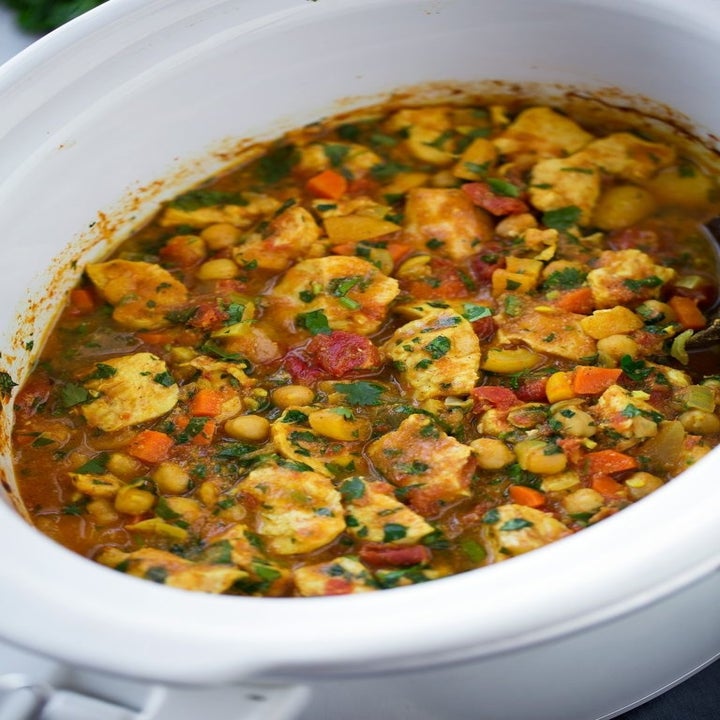 A slow cooker filled with chickpea chicken tagine with diced vegetables and herbs.