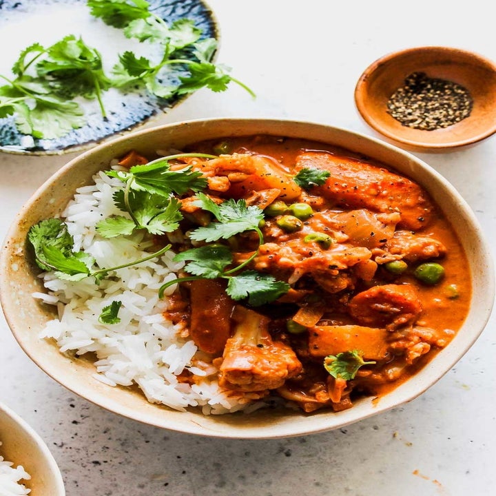 A bowl of cauliflower, carrot, and peas in tikka masala sauce over rice with fresh cilantro.