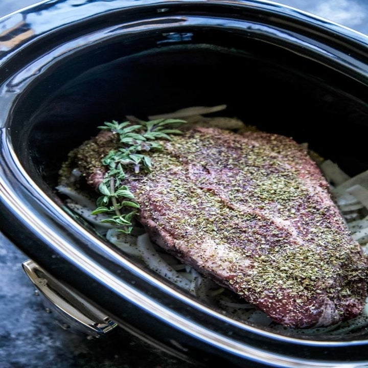 Beef chuck roast in the slow cooker topped with spices and herbs.