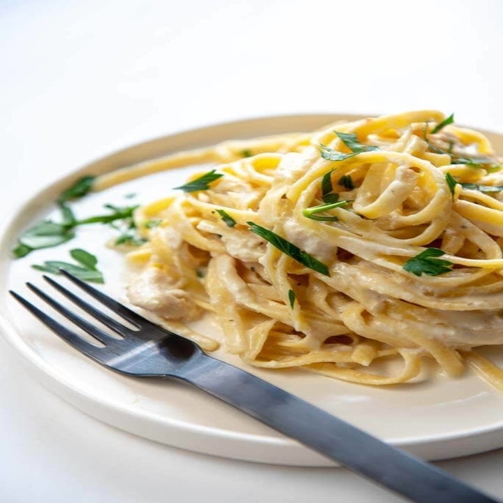 A plate of cheesy, creamy pasta with shredded chicken and fresh herbs.