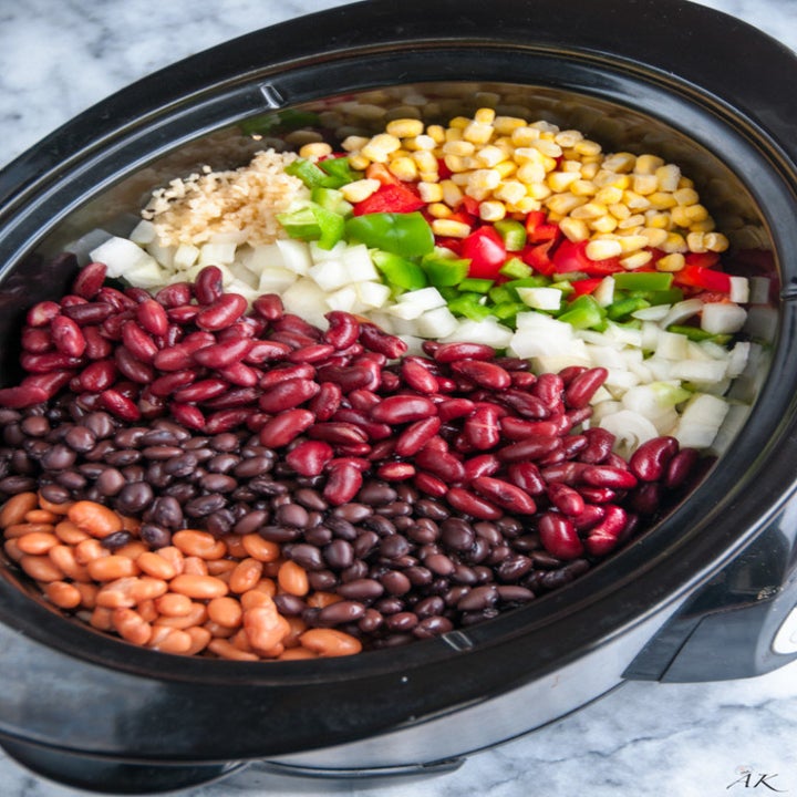 Ingredients for bean chili in a crock pot with three kinds of beans, corn, onion, pepper, and spices.