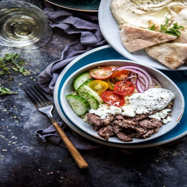 A Greek gyro bowl with chopped cucumbers, tomatoes, red onion, and Tzatziki with pita bread on the side.