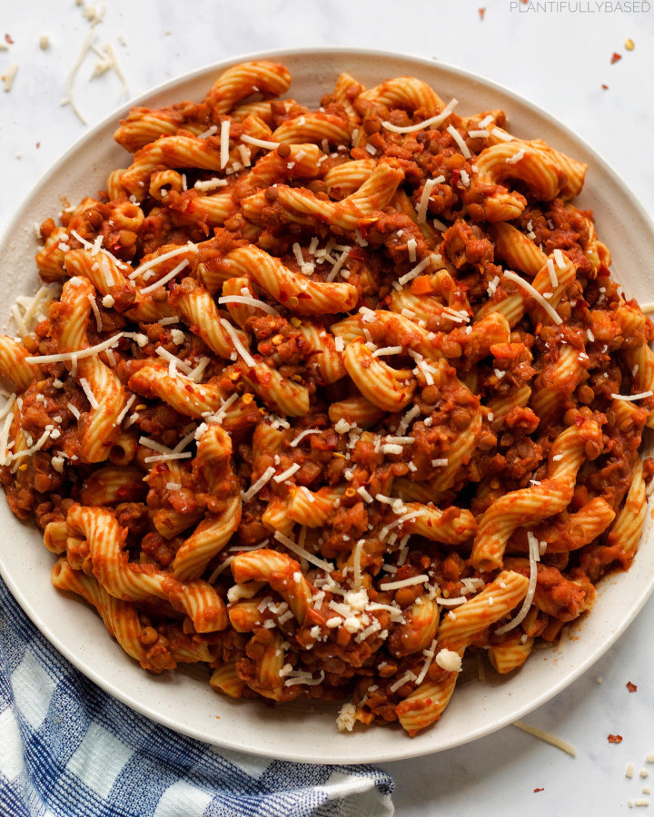 A plate of pasta with lentil Bolognese sauce and shredded Parmesan cheese.