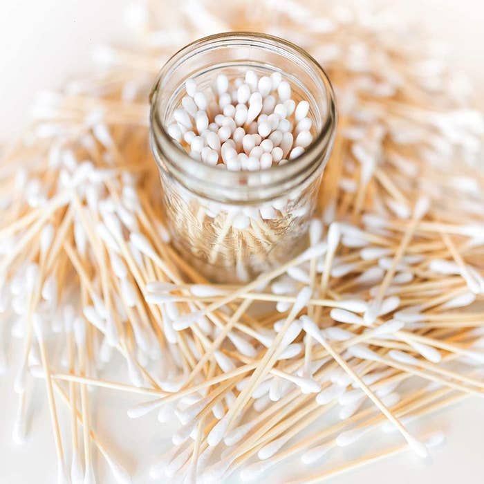 A close up of a jar full of bamboo cotton swabs surrounded by more cotton swabs