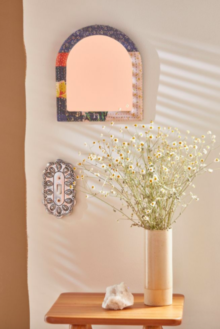Decorative metal light switch cover next to wooden table with a vase of flowers and a crystal