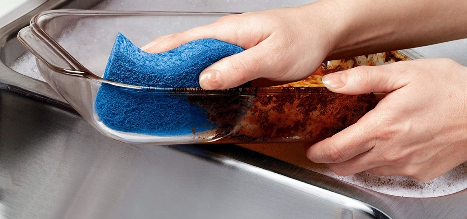 A person using the sponge on a dish removing stains