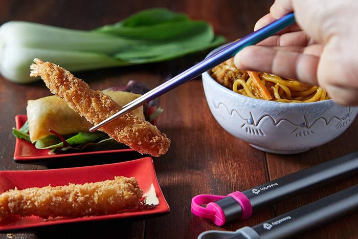 A person using the chopsticks to pick up a piece of tempura