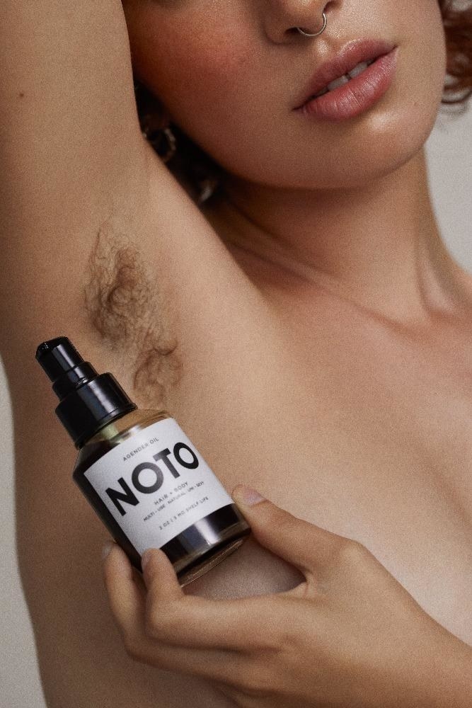 model holding oil bottle against hairy underarm 