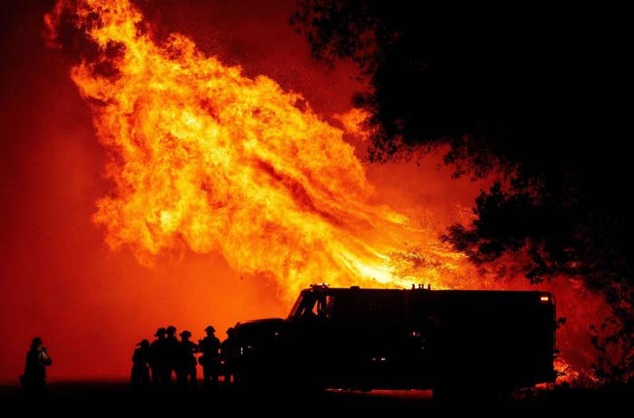 A large blaze towers overhead as five firefighters crowd by their truck