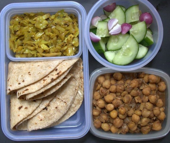 A plastic lunch box containing some roti, cabbage sabzi, chickpea sabzi and a salad of cucumber and onions