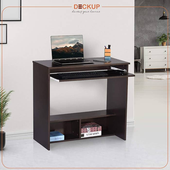A wooden desk with a keyboard kept on the sliding drawer and a laptop on top.