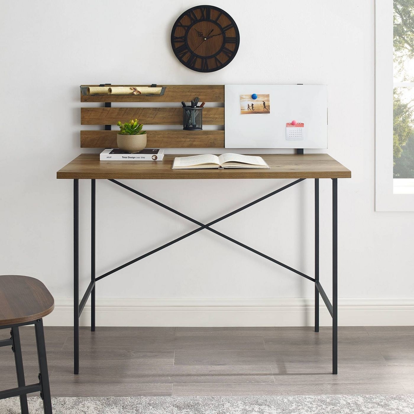 A wooden desk with black metal legs and a decorative packing against the wall for hanging photos or organizing items