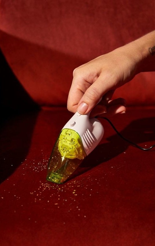 A hand holding a minaiture handheld vacuum cleaning up glitter.