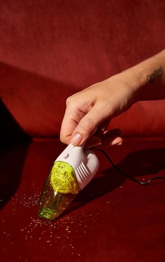 A hand holding a minaiture handheld vacuum cleaning up glitter.