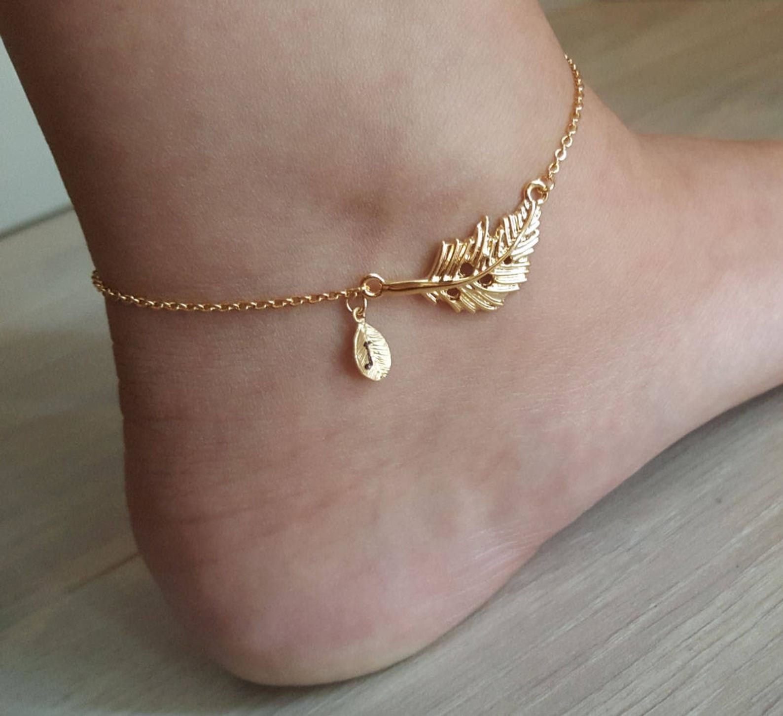A foot wearing the gold anklet with a large leaf and a small leaf with an initial &quot;J&quot;