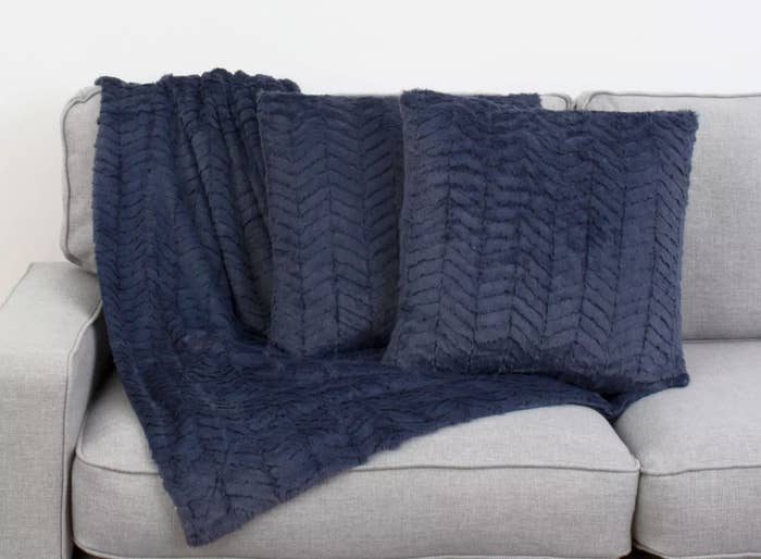 A navy throw blanket under two navy chevron throw pillows on a grey couch