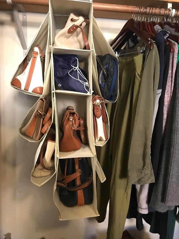 Reviewer pic of the fabric hanger in a closet with four full compartments in the center and three cradled off of each side with purses and bags in all of them. 