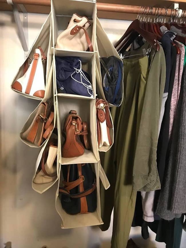 Reviewer pic of the fabric hanger in a closet with four full compartments in the center and three cradled off of each side with purses and bags in all of them. 