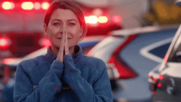 Meredith praying in front of a backdrop of sirens and emergency lights