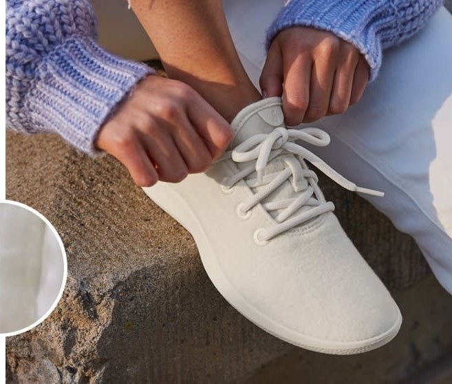Model wearing the sneakers with thicker fabric in white, with white soles and laces.