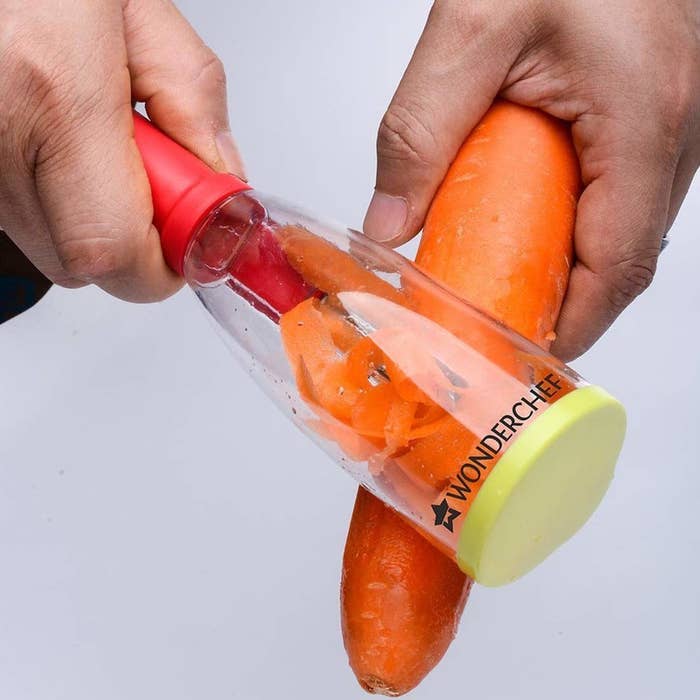 A carrot being peeled with the smart peeler. It has a lid and handle to avoid direct contact with the blade.