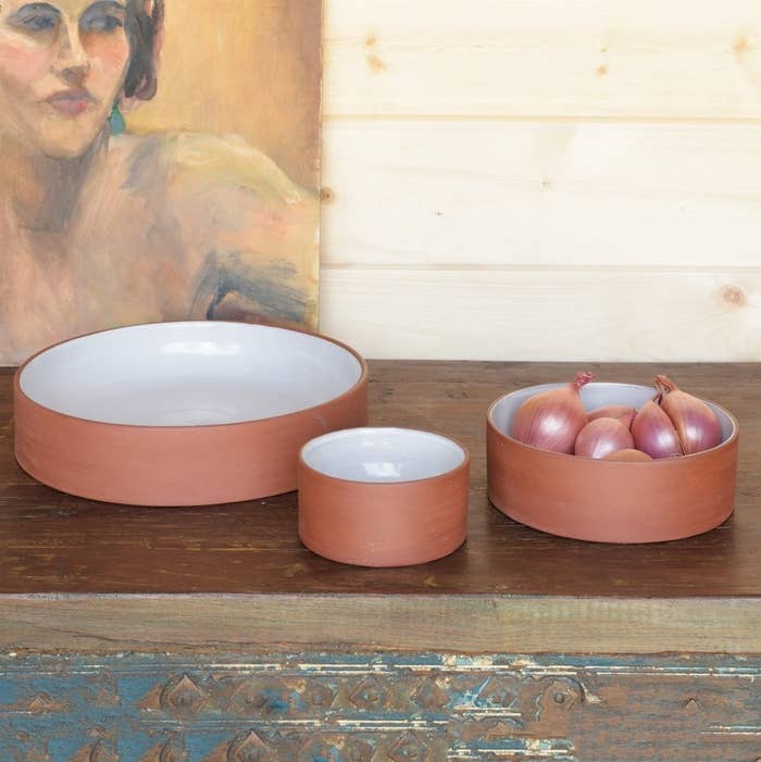 three sizes of flat-bottom vertical wall shallow bowls that are terracotta on the outside and white on the inside with onions in one