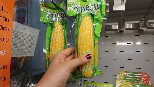 A shrink-wrapped corn on the cob hanging in the refrigerated section of 7-Eleven