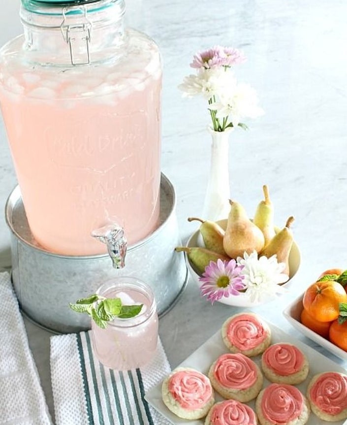 Clear glass drink dispenser with teal lid filled with pink lemonade