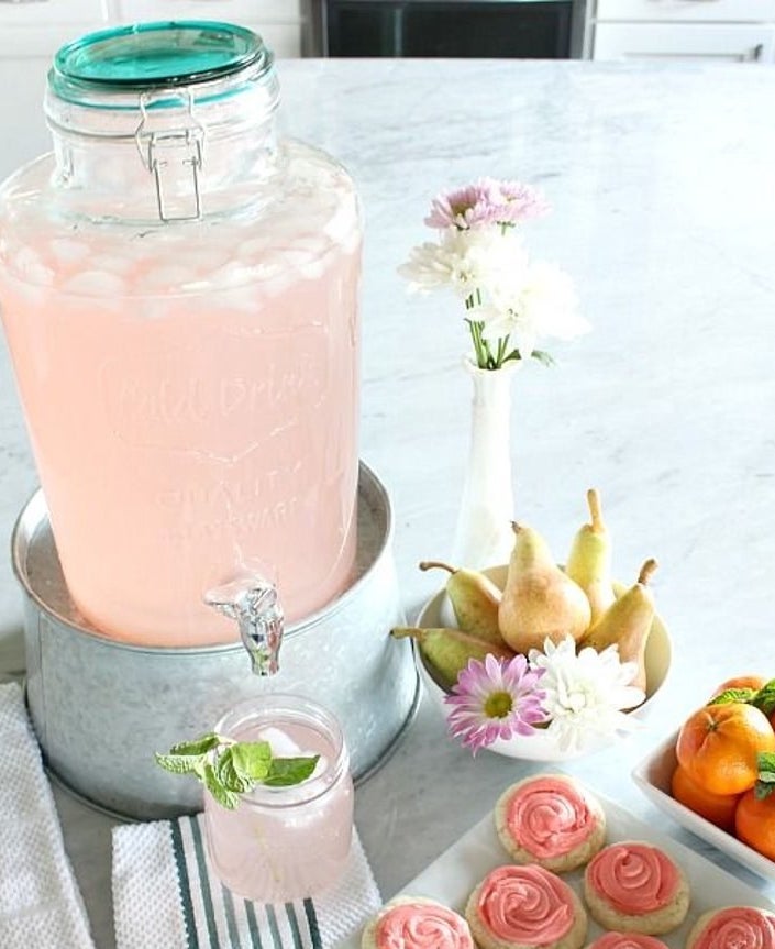 Clear glass drink dispenser with teal lid filled with pink lemonade