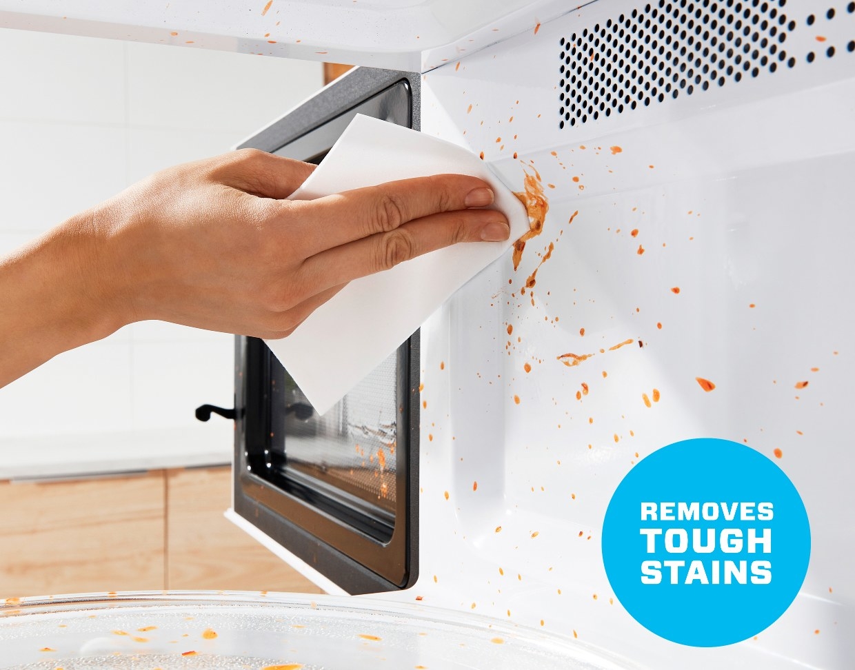 A hand removing tough stains from the microwave with a Magic Eraser cleaning sheet