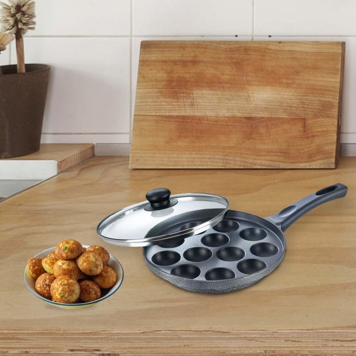 A paniyarakkal pan on a kitchen platform with a plate of appams.