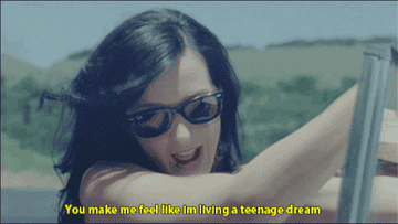 A GIF of Katy Perry standing in a convertible singing &quot;You make me feel like I&#x27;m living a teenage dream&quot;