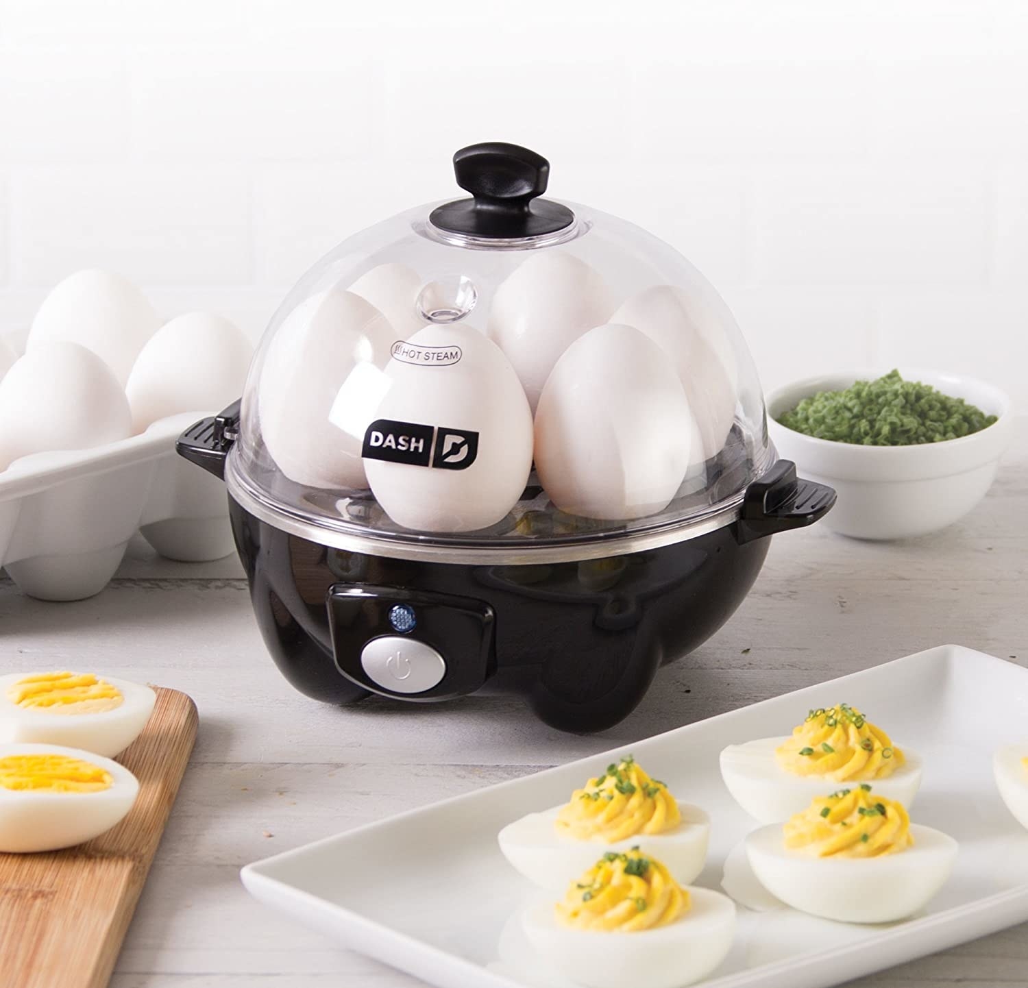 An egg cooking machine with six eggs in it and deviled eggs in the foreground