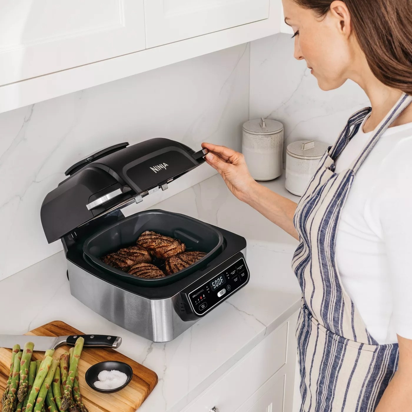A model checking the four steaks cooking on her Ninja indoor grill and air fryer